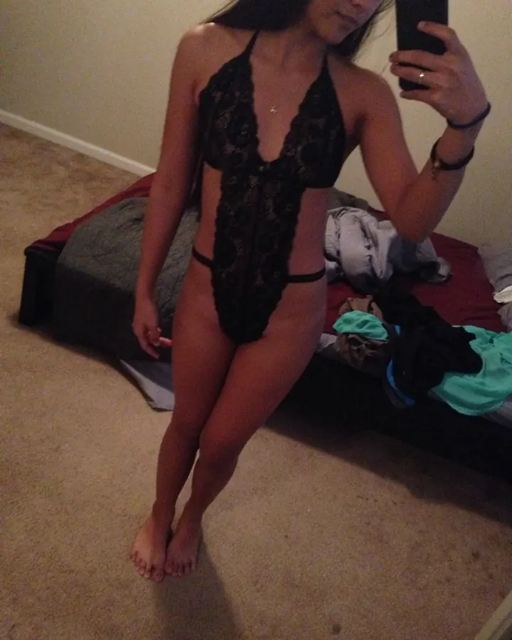 Femme prenant un selfie devant un miroir, portant un body en dentelle noire, dans une chambre.
