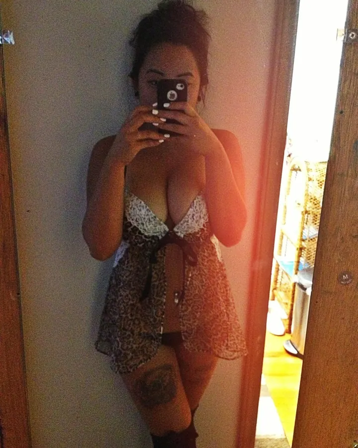 Femme prenant un selfie devant un miroir, portant une robe léopard et un soutien-gorge blanc, avec un tatouage au mollet.