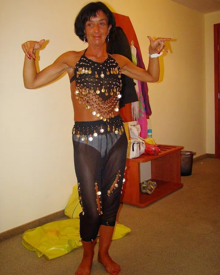 Femme arabe en tenue de danse orientale, souriante, pointant vers elle-même.