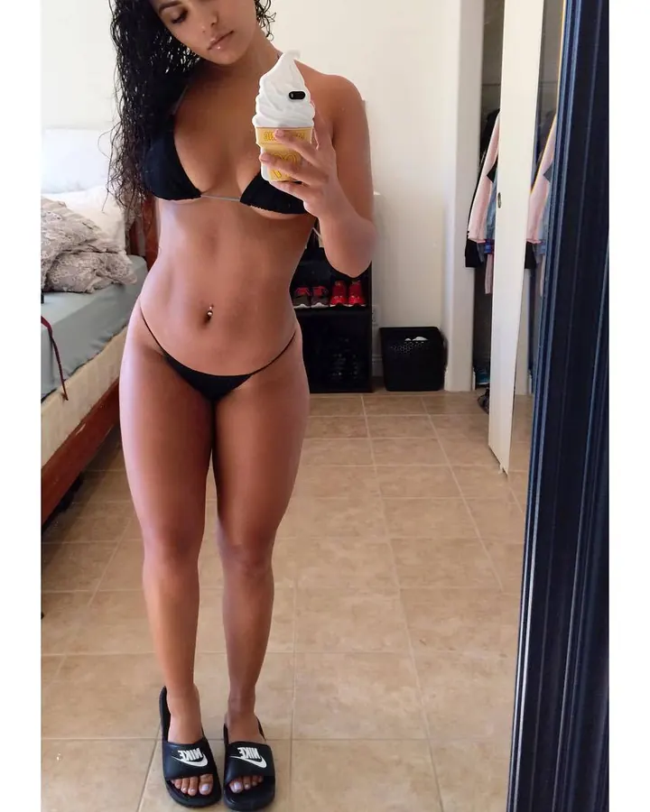 Femme arabe de 25-35 ans, cheveux bruns-noirs, portant un bikini noir, tenant un cornet de glace.