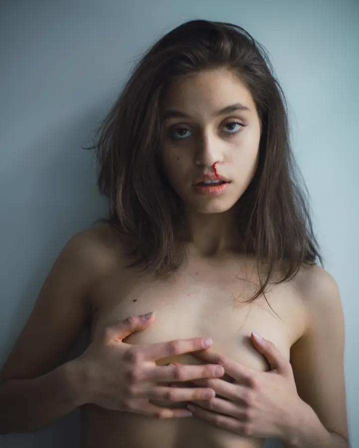 Jeune femme arabe aux yeux noirs, cheveux châtains, portant un string noir, debout près d'un mur blanc.