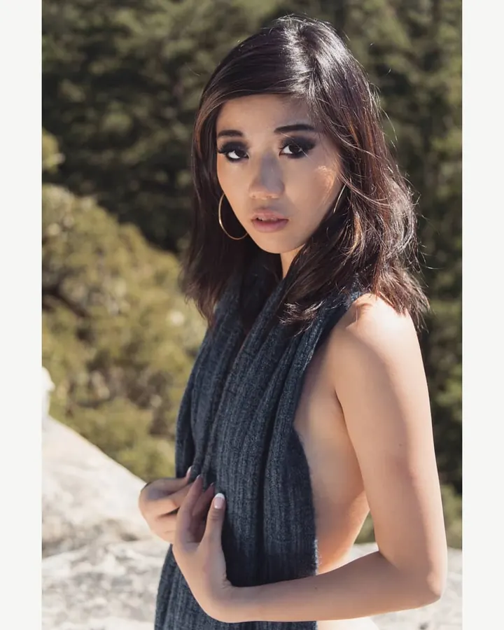 Femme arabe de 25-35 ans, cheveux châtains, portant un string noir, debout près d'un mur blanc.
